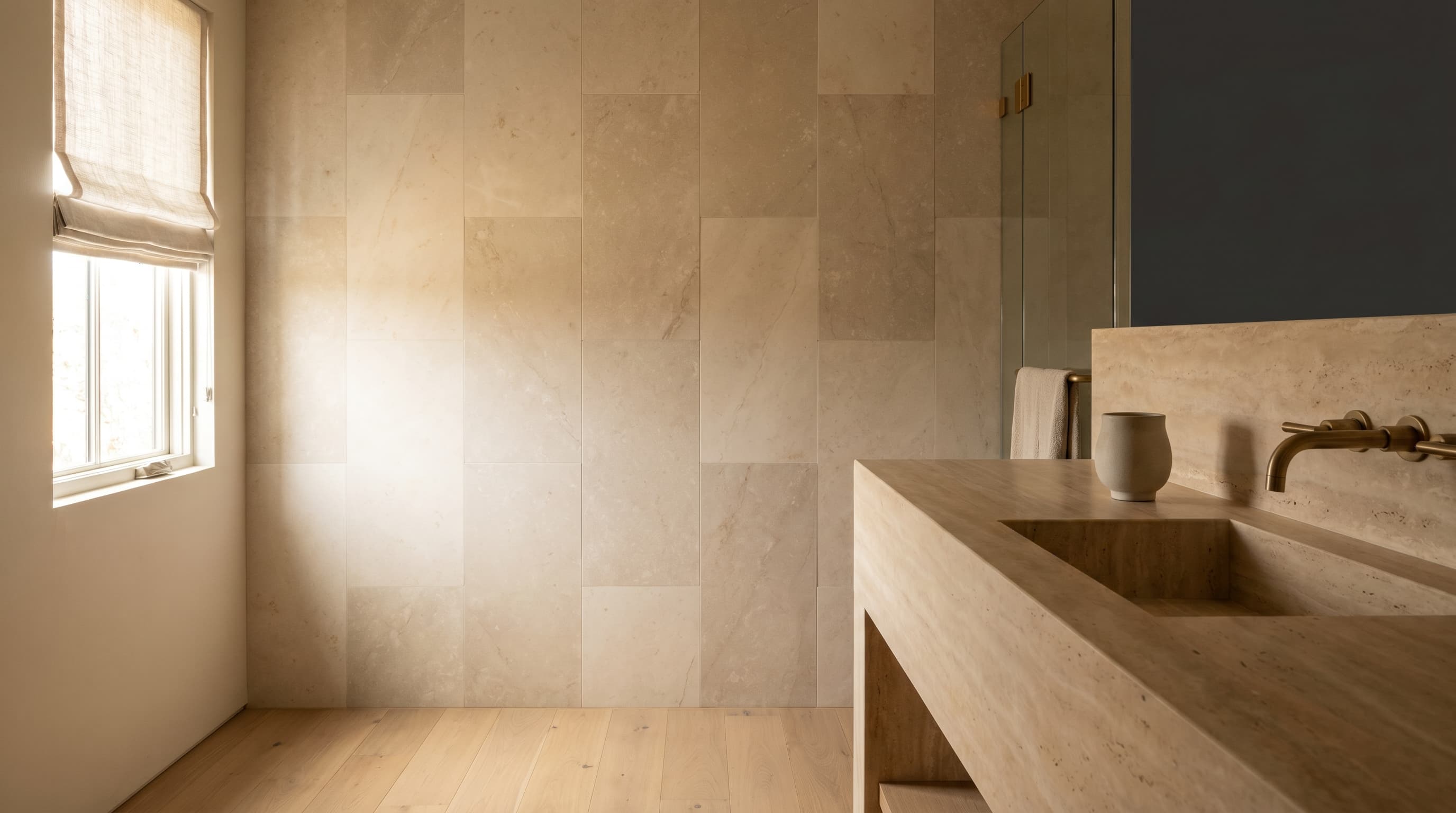 Finished San Diego County bathroom with a stacked warm-stone tile wall, freestanding stone vanity, and unlacquered brass fixtures